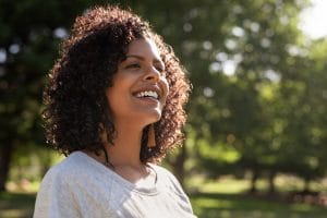 Young woman with curly hair smiling while standing outside in a park on a sunny summer afternoon