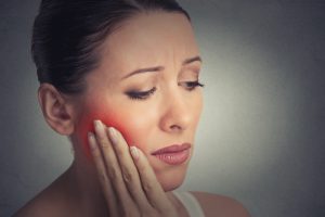 Closeup portrait young woman with sensitive tooth ache crown problem about to cry from pain touching outside mouth with hand isolated grey wall background. Negative emotion facial expression feeling