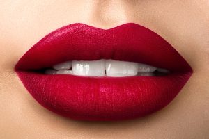 Close up view of beautiful woman lips with red matt lipstick. Open mouth with white teeth. Cosmetology, drugstore or fashion makeup concept. Beauty studio shot. Passionate kiss