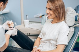 friendly doctor dentist examine teeth of caucasian young woman in casual wear, isolated in dentist office, using special medical equipment